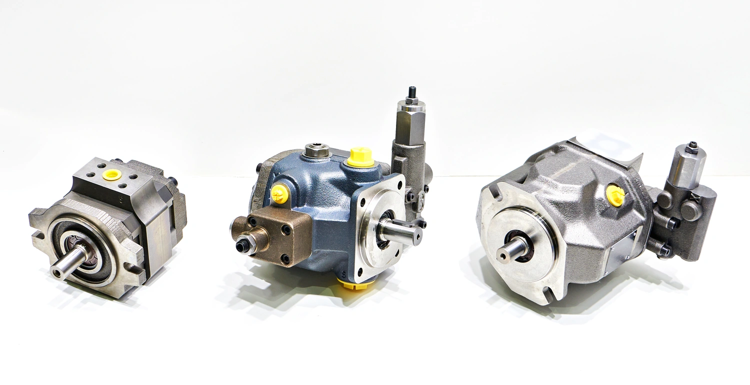 Three hydraulic pumps with metallic finishes and yellow accents, displayed on a white background, showcasing their design and components.
